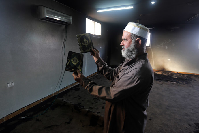 A Palestinian Muslim cleric holds up a burnt copy of the Koran, Islams holy book, in a mosque allegedly burnt by Jewish settlers, in the village of Aqraba, in the Israeli occupied Palestinian West Bank, near the northen city of Nablus, on October 14, 2014. (AFP Photo / Jaafar Ashtiyeh)