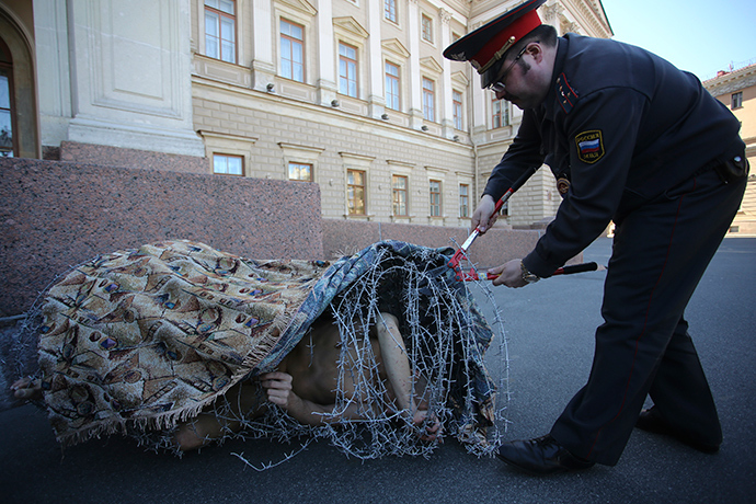 Artist Pyotr Pavlensky lies on the ground, wrapped in barbed wire roll, during a protest action in St. Petersburg May 3, 2013 (Reuters / Artur Bainozarov)