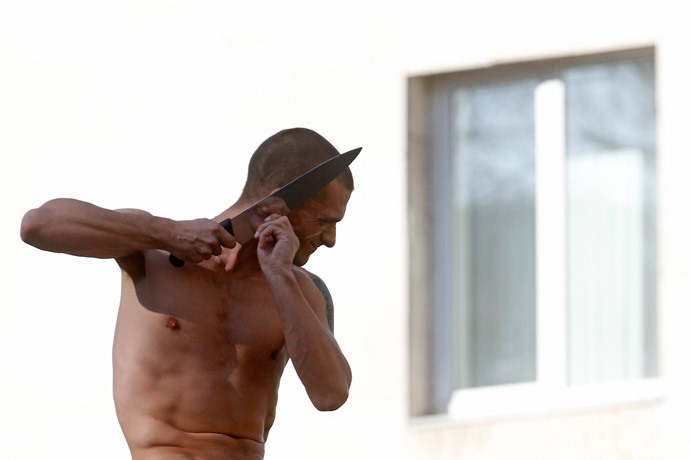 Artist Pyotr Pavlensky cuts off a part of his earlobe while sitting on the wall enclosing the Serbsky State Scientific Center for Social and Forensic Psychiatry during his protest action titled "Segregation" in Moscow October 19, 2014. (Reuters / Maxim Zmeyev)