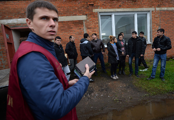 An officer of the Federal Migration Service, left, holds documents of foreign workers during a raid conducted by the Federal Migration Service to identify illegal migrants (RIA Novosti/Maksim Blinov)