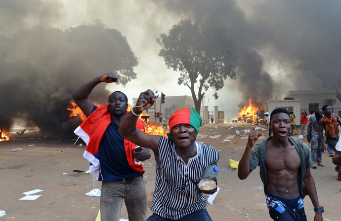 Men shout slogans in front of burning cars, near the Burkina Faso's Parliament where demonstrators set fire, on October 30, 2014 in Ouagadougou, as they protest against plans to change the constitution to allow President Blaise Compaore to extend his 27-year rule. (AFP Photo/Issouf Sango)