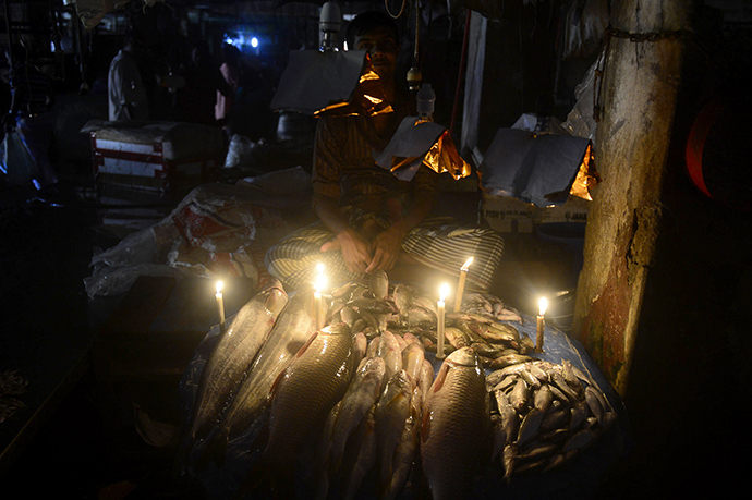 A Bangladesh fishmonger lights his fish stall with candles during a power blackout in Dhaka on November 1, 2014 (AFP Photo / Munir uz Zaman)