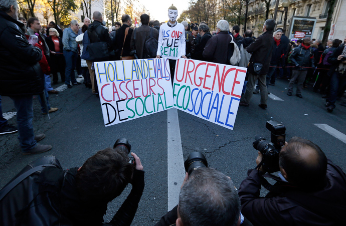 Photographers take pictures of a man wearing a "Guy Fawkes" mask and holding placards that read, "Hollande and Valls, you are social breakers" (L) and "Emergency eco sociale", during a demonstration against the government's austerity reforms, in Paris November 15, 2014 (Reuters / Gonzalo Fuentes)