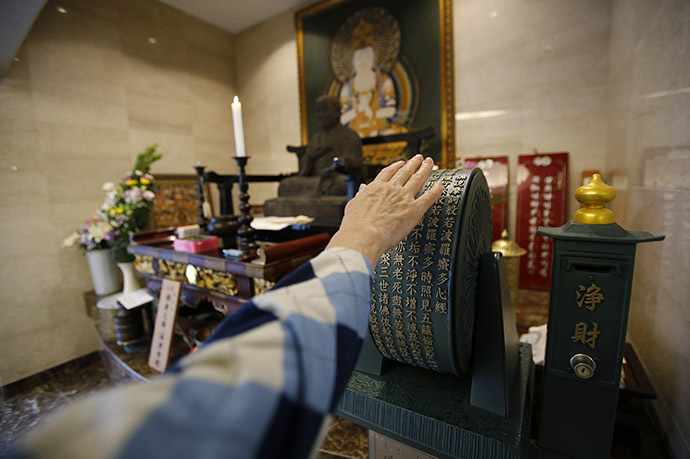 A visitor spins a prayer wheel in front of a Buddhist statue in the lobby of Ryogoku Ryoen, a multi-storey vault-style graveyard equipped with modern tombs that robotically retrieves the correct tombstone or urn based on which identity card is provided, in downtown Tokyo October 27, 2014. (Reuters/Toru Hanai)
