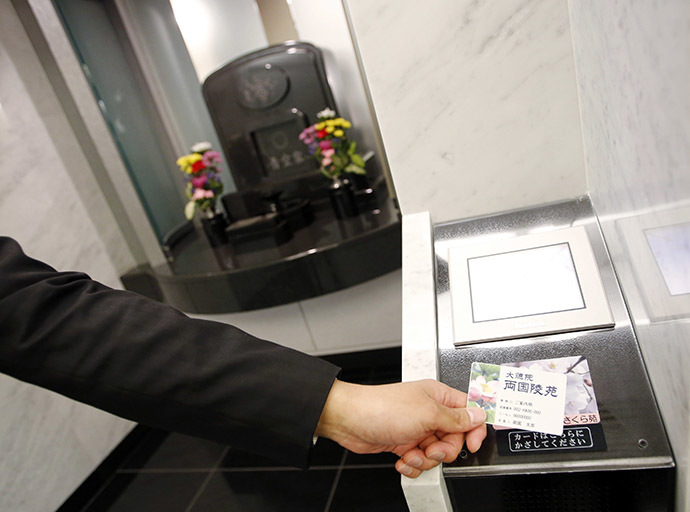 A staff member demonstrates how to use a modern tomb that robotically retrieves the correct tombstone or urn based on which identity card is provided, at Ryogoku Ryoen, a multi-storey vault-style graveyard, in downtown Tokyo October 27, 2014. (Reuters/Toru Hanai)
