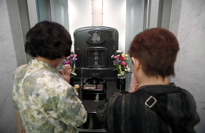 Yukiko Kimura (R) prays for her late husband Mitsugi with Mitsugi's sister Kiyoko Matsuura in front of a modern tomb that robotically retrieves the correct tombstone or urn based on which identity card is provided, at Ryogoku Ryoen, a multi-storey vault-style graveyard, in downtown Tokyo October 27, 2014. (Reuters/Toru Hanai)