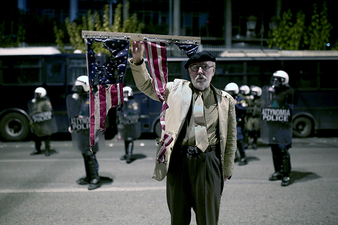 A man holds a burnt US flag in front of the US embassy on November 17, 2014 in the centre of Athens at a march commemorating the 1973 students uprising against the military junta. (AFP Photo / Angelos Tzortzinis)