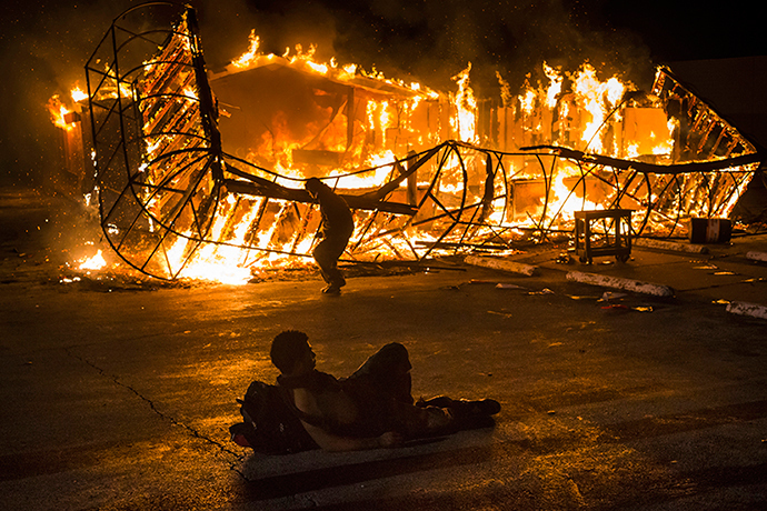 A resident, lying shirtless, keeps warm as another approaches the blazing skeleton of Juanita's Fashions R Boutique after it was burned to the ground in Ferguson, Missouri early morning November 25, 2014 (Reuters / Adrees Latif)