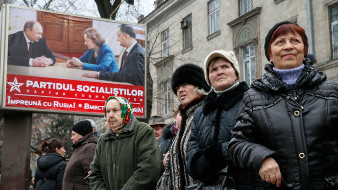 People walk near a pre-election poster for the Party of Socialists, with a picture of party members meeting with Russian President Vladimir Putin, in Chisinau November 29, 2014. (Reuters / Gleb Garanich )