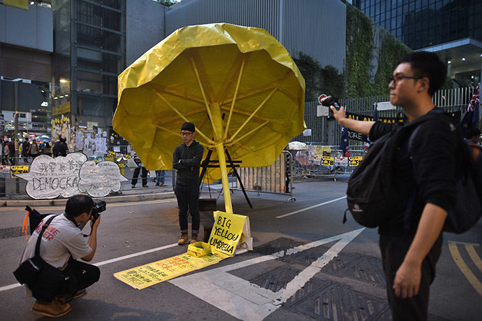 A man poses for a photograph under a yellow umbrella, a symbol of the pro-democracy protests, in the Admiralty district of Hong Kong on November 30, 2014. (AFP Photo/Philippe Lopez)