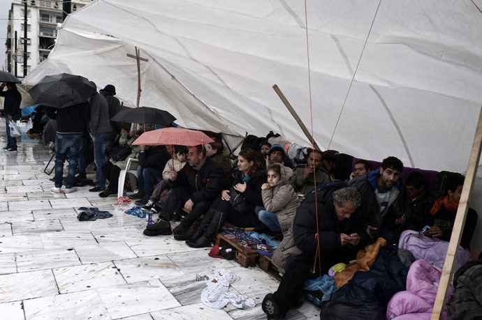 Syrian refugees sit under a makeshift tent as they take cover from the heavy rain during a protest in Athens on December 12, 2014. (AFP Photo)