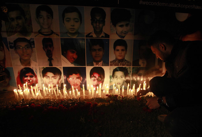 A man places a rose after lighting candles in front of portraits of the victims of the Taliban attack on the Army Public School in Peshawar, during a candlelight vigil in Lahore December 19, 2014. (Reuters/Mohsin Raza)