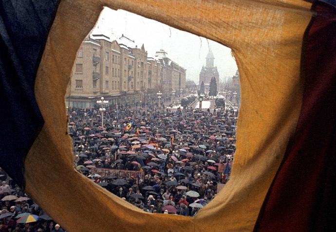 File photo of citizens, seen through a flag with the communist coat of arms torn off, demonstrating against Ceausescu in front of the Opera building December 23, 1989. (Reuters/Petar Kujundzic)