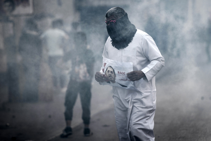A Bahraini protestor takes cover from tear gas during clashes with riot police following a protest against the arrest of the head of the banned Shiite opposition movement Al-Wefaq, Sheikh Ali Salman (on the poster) on January 1, 2015 in Bilad al-Qadeem, a suburb of Manama. (AFP Photo / Mohammed Al-Shaikh)