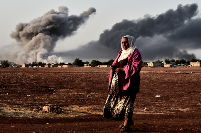 A woman walk as smoke rises behind her, from the the Syrian town of Ain al-Arab, known as Kobane by the Kurds, after a strike from the US-led coalition as it seen from the Turkish - Syrian border in the southeastern village of Mursitpinar, Sanliurfa province (AFP Photo / Aris Messinis)