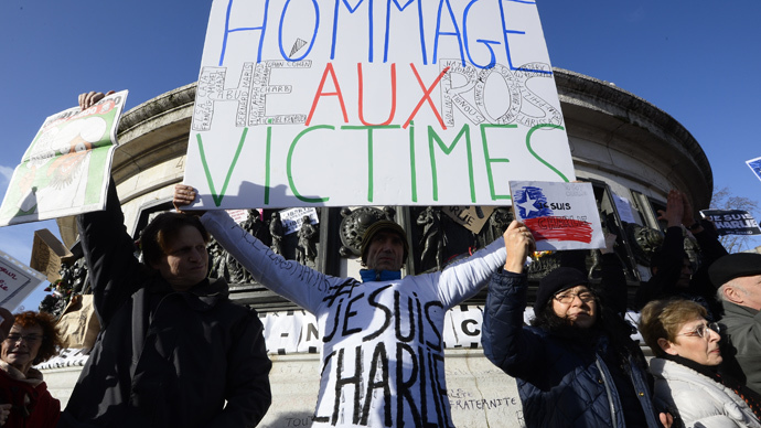 A man holds a cardboard reading "Hommage to the Victims-Heros" as people gather on the Place de la Republique (Republic Square) in Paris before the start of a Unity rally âMarche Republicaineâ on January 11, 2015 (AFP Photo / Bertrand Guay)