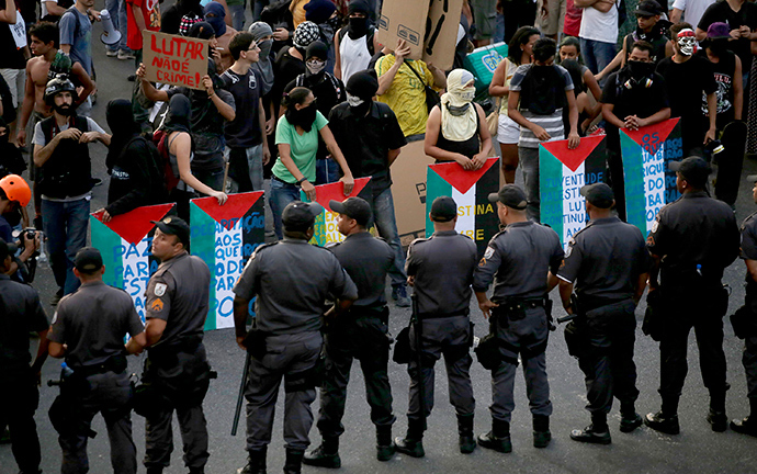Riot police block a street as demonstrators use makeshift shields painted with the colours of the Palestinian flag during a protest against fare hikes for city buses in Rio de Janeiro January 16, 2015 (Reuters / Mauro Pimentel)