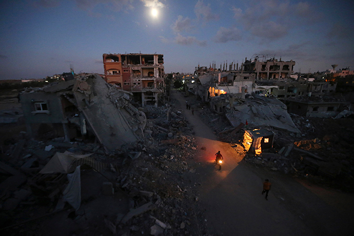 Palestinian pedestrians and a motorcyclist commute along a road between ruins of houses, which witnesses said were damaged or destroyed during the Israeli offensive, in Beit Hanoun town in the northern Gaza Strip in this September 7, 2014 file photo (Reuters / Mohammed Salem)