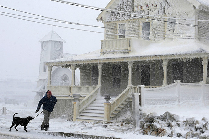 A man walks his dog past an ocean front house covered in ice during a winter blizzard in Marshfield, Massachusetts January 27, 2015. (Reuters/Brian Snyder)