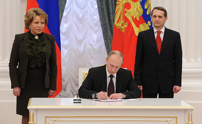 Russian President Vladimir Putin (C) signs documents as Sergey Naryshkin (R), speaker of the State Duma, Russia's lower parliament house, and Valentina Matviyenko, head of the Federation Council, look on during a ceremony in Moscow's Kremlin March 21, 2014 (RIA Novosti / Mikhail Klimentyev)