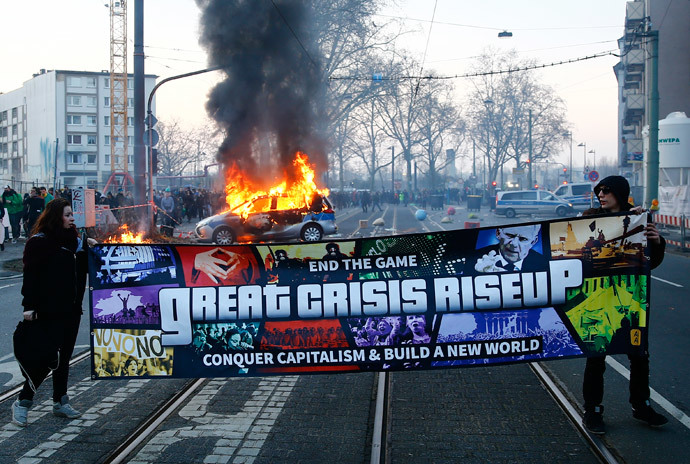 Anti-capitalist protesters pose in front of a burning German police car that was set on fire in the early morning hours near the European Central Bank (ECB) building before the official opening of its new headquarters in Frankfurt March 18, 2015. (Reuters / Kai Pfaffenbach)