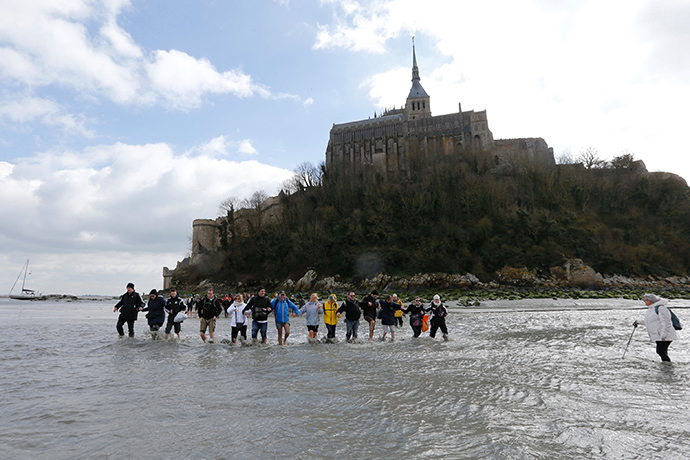 Tourists walk through retreating waters with a bay guide around the Mont Saint-Michel 11th century abbey off France's Normandy coast March 21, 2015 (Reuters / Pascal Rossignol)