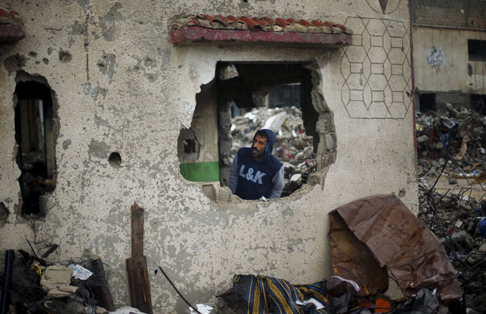 A Palestinian man takes cover inside the remains of a house that witnesses said was destroyed by Israeli shelling during a 50-day war in 2014 summer, on a rainy day in Beit Hanoun town in the northern Gaza Strip April 12, 2015. (Reuters/Suhaib Salem)