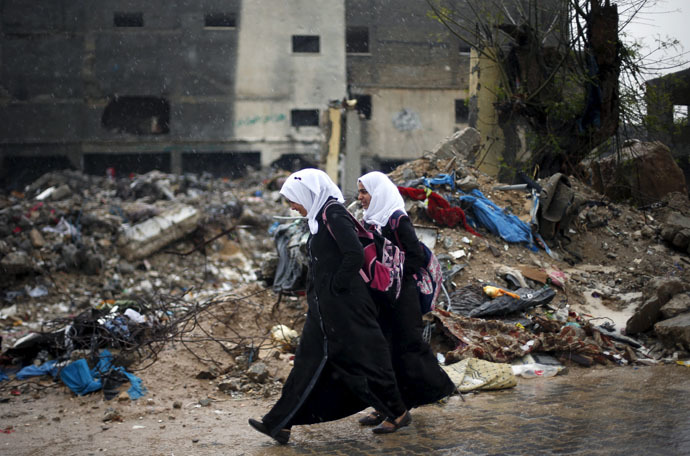 Palestinian schoolgirl walk past the rubble of a house that witnesses said was destroyed by Israeli shelling during a 50-day war in 2014 summer, on a rainy day in Beit Hanoun town in the northern Gaza Strip April 12, 2015. (Reuters/Suhaib Salem)