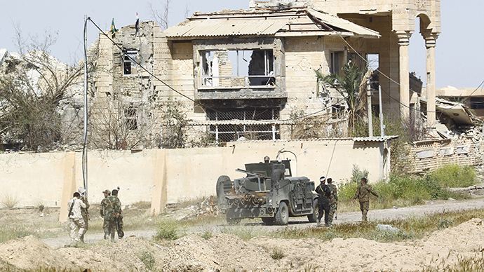 Iraqi security forces and Shi'ite paramilitary fighters walk near a destroyed building in Tikrit (Reuters / Alaa Al-Marjani)