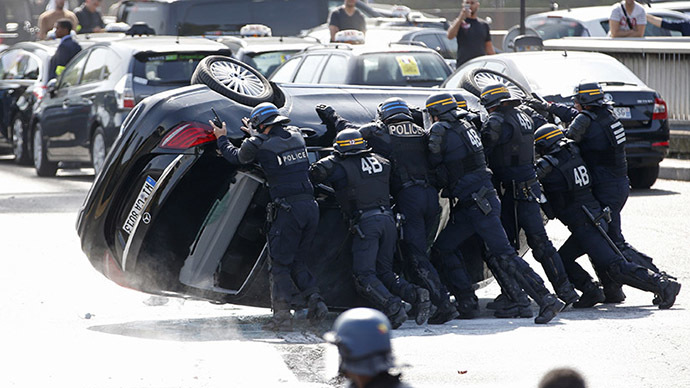 French riot police push an overturned car as striking French taxi drivers demonstrate at the Porte Maillot to block the traffic on the Paris ring road during a national protest against car-sharing service Uber, in Paris, France, June 25, 2015. (Reuters / Charles Platiau)