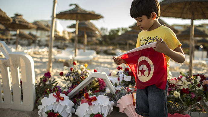 A boy holds a Tunisian flag as he stands near bouquets of flowers laid at the beachside of the Imperiale Marhabada hotel, which was attacked by a gunman in Sousse, Tunisia, June 27, 2015 (Reuters / Zohra Bensemra)