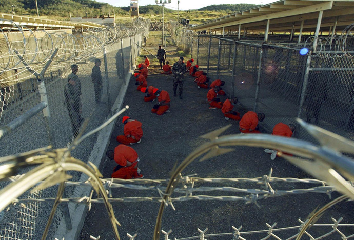 Detainees in orange jumpsuits sit in a holding area under the watchful eyes of military police during in-processing to the temporary detention facility at Camp X-Ray of Naval Base Guantanamo Bay in this January 11, 2002 file photograph. (Reuters/Stringer/Files)