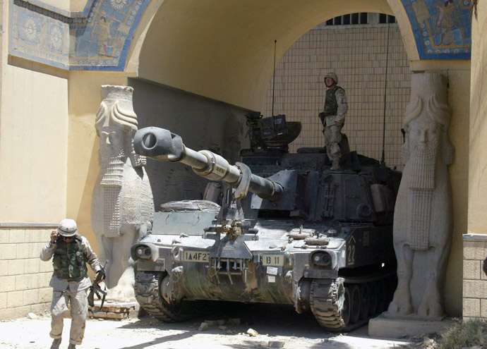 A US soldier stands on a Bradley tank stationed at the main enterance of the National Museum as another soldier walks by in Baghdad 21 June 2003. (AFP Photo)