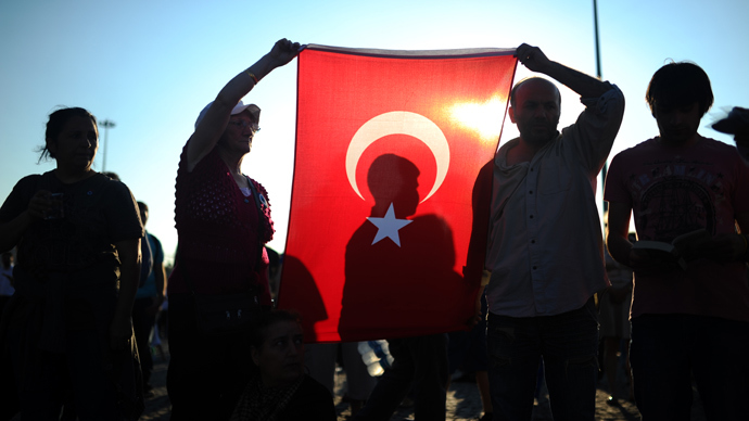 People hold a Turkish national flag as they stand on the flashpoint Taksim square in Istanbul on June 18, 2013 during a wave of new alternative protests (AFP Photo / Bulent Kilic) 