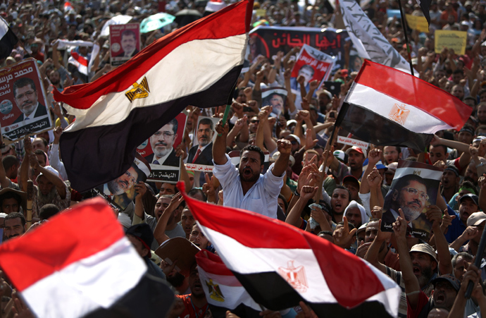 Egyptian supporters of deposed president Mohamed Morsi (portrait) wave their national flag as they attend a rally in support of the former Islamist leader outside Cairo's Rabaa al-Adawiya mosque on July 8, 2013 (AFP Photo / Mahmud Hams) 