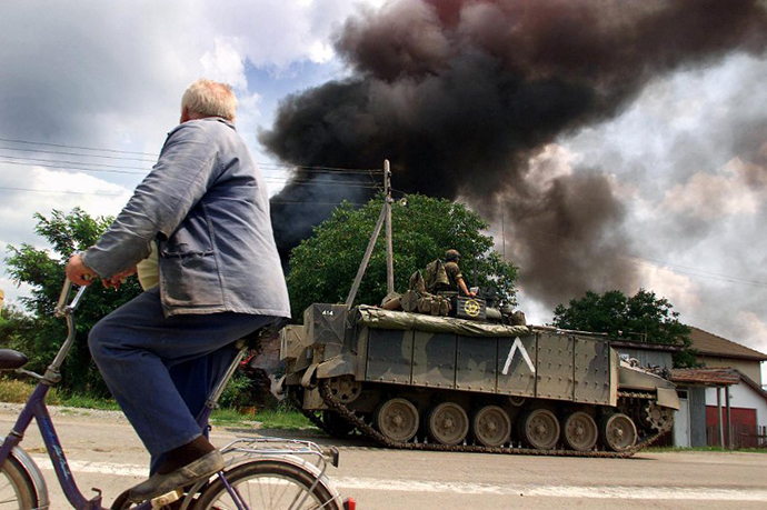 A resident rides 03 July 1999 past Serb-owned burning house in Kosovksa Mitrovica. (AFP Photo / Jean-Philippe Ksiazek)