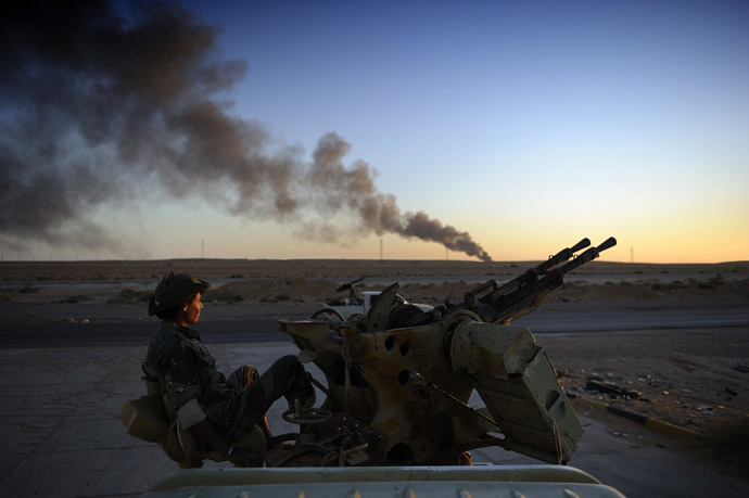 A rebel fighter looks on as he sits on an anti-aircraft machine gun on August 29, 2011 near Ras Lanuf while smoke pours from a rafinery. (AFP Photo)