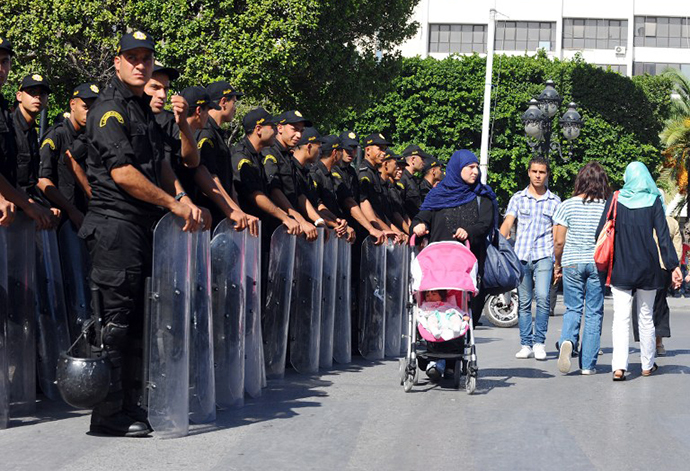 Tunisian people walk past security forces outside the Interior ministry on Tunis' central Habib Bourguiba Avenue where a demonstration takes place on October 23, 2013 to demand the resignation of Tunisia's Islamist-led government, ahead of a national dialogue aimed at ending months of political deadlock. (AFP Photo / Fethi Belaid)
