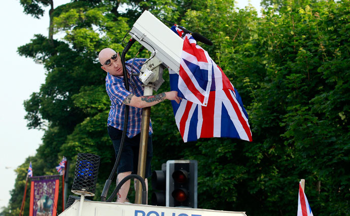 A man covers a surveillance camera with a Union flag after climbing on top of an armoured police Land Rover.(Reuters / Cathal McNaughton)
