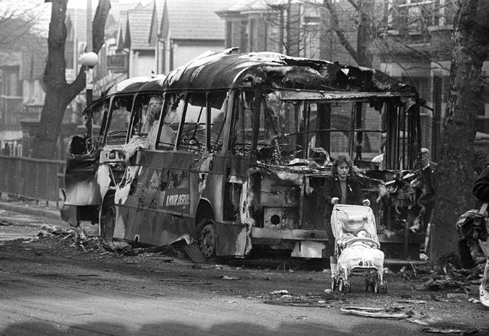 A woman pushes her baby carriage past a burnt bus in West Belfast set on fire March 16, 1988 after three people were killed by a gunfire and grenade attack during funerals for the IRA guerrillas killed in Gibraltar in this undated image. (Reuters)