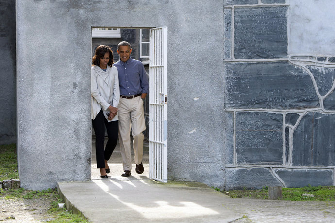US President Barack Obama (R) and First Lady Michelle Obama walk through a prison yard as they tour Robben Island where South-African anti-apartheid activist Nelson Mandela, was once jailed, on June 30, 2013. (AFP Photo / Saul Loeb)
