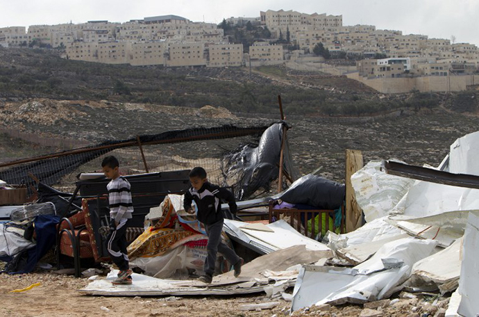 Palestinian children walk through the rubble of a house demolised by the Israeli authorities for being built without municipal permission in the Arab east Jerusalem neighborhood of Beit Hanina on January 27, 2014, with the Jewish settlement of Ramat Shlomo in the background. (AFP Photo / Ahmad Gharabli)