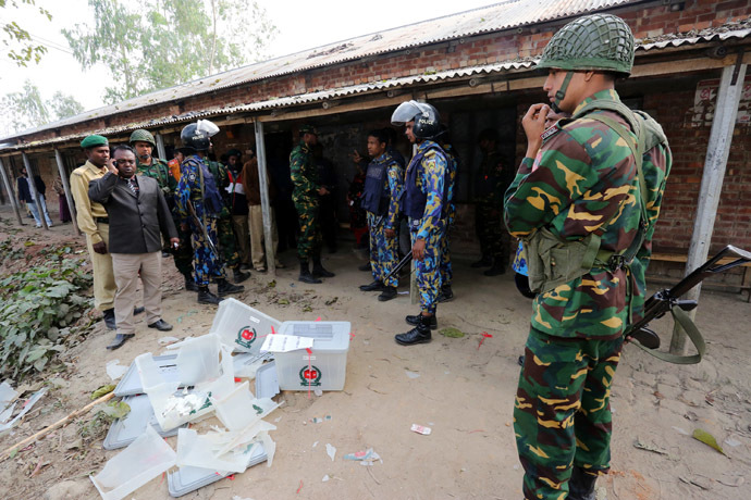 Bangladeshi police and soldiers stand next to damaged ballot boxes in front of a polling station after it was attacked by protestors in the northern town of Bogra on January 5, 2014. (AFP Photo)
