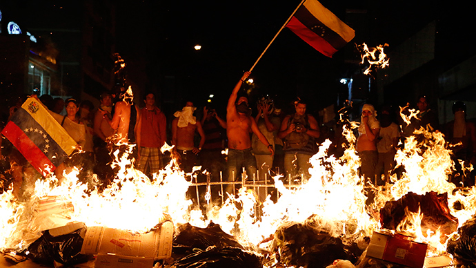 Opposition demonstrators hold a Venezuelan flag in front of a burning barricade during a protest against President Nicolas Maduro's government in Caracas February 15, 2014 (Reuters / Carlos Garcia Rawlins)