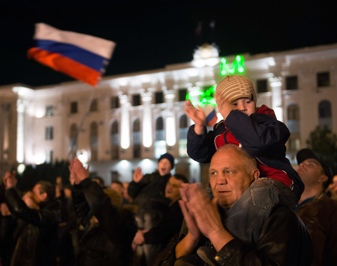 A young boy sitting on the shoulders of an elderly man claps as people watch fire works in the center of the Crimean city of Simferopol on March 21, 2014. (AFP Photo)