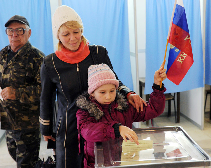A child casts her mother's ballot while holding a Russian flag at a polling station on March 16, 2014 in Simferopol. (AFP Photo / Viktor Drachev)
