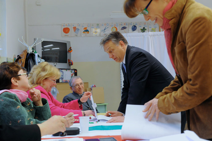 Hungarian Prime Minister Viktor Orban (C) chats with an election officals as his wife Aniko Levai (R) holds ballot papers in a polling station of a local school at12th district of Budapest on April 6, 2014.(AFP Photo / Attila Kisbenedek)