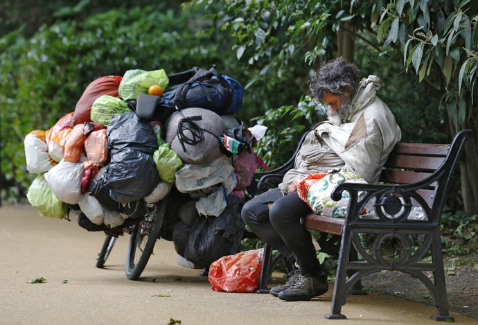 A homeless man sleeps on a park bench next to a bicycle with bags of his belongings in London (Reuters//Luke MacGregor)