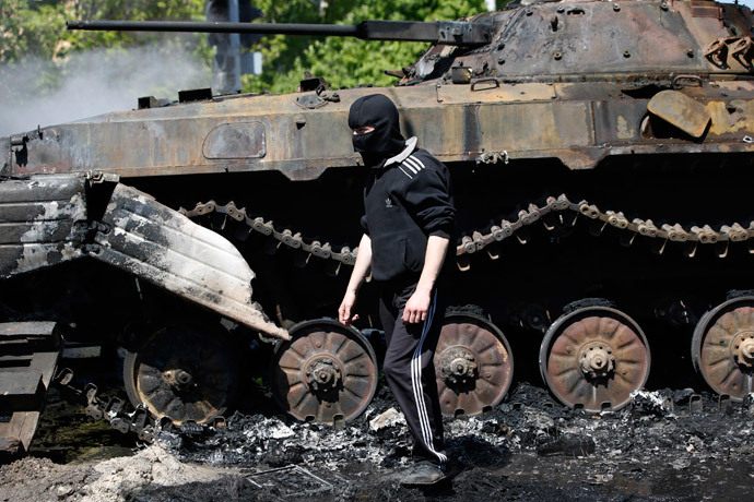 A masked man walks past a burnt-out armoured personal carrier near the city hall in Mariupol, eastern Ukraine May 10, 2014.(Reuters / Marko Djurica )
