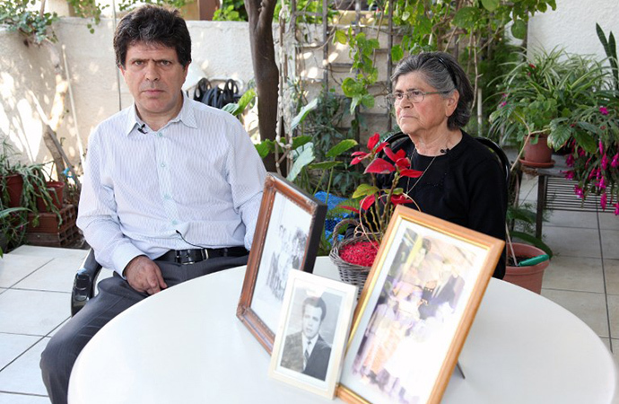 Greek Cypriot Marios Kouloumas poses near his mother, on February 14, 2014 in Nicosia, with pictures of his father who is one of hundreds of Greek and Turkish Cypriots who disappeared during a decade of unrest culminating in the Turkish invasion of 1974. (AFP Photo / Barbara Laborde)